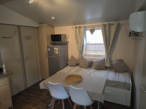 Une pièce de taille modeste comprenant un lit, deux chaises, une petite table, un réfrigérateur, un four à micro-ondes et une fenêtre avec des rideaux.
