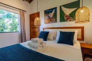 A neatly made bed with rolled towels, a wooden headboard, and artwork on the wall.