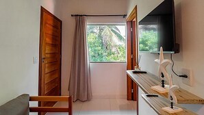 Una habitación con puerta de madera, ventana con vista a follaje y televisor de pantalla plana montado en la pared, además de un banco de madera.