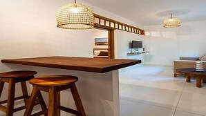 Cocina moderna con barra de madera, dos taburetes e iluminación colgante.