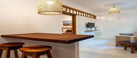 A modern kitchen with a wooden bar counter, two stools, and pendant lighting.