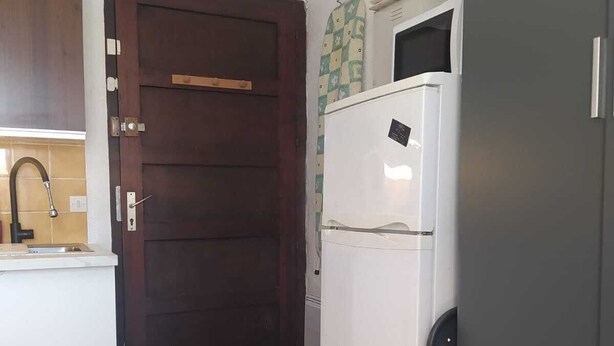 A kitchen with a dark wooden door, a white refrigerator, and a tiled backsplash. - Studio apartment in a residential complex on the edge of a pond (Le Barcarès)