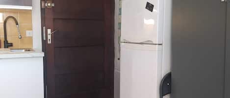 A kitchen with a dark wooden door, a white refrigerator, and a tiled backsplash.