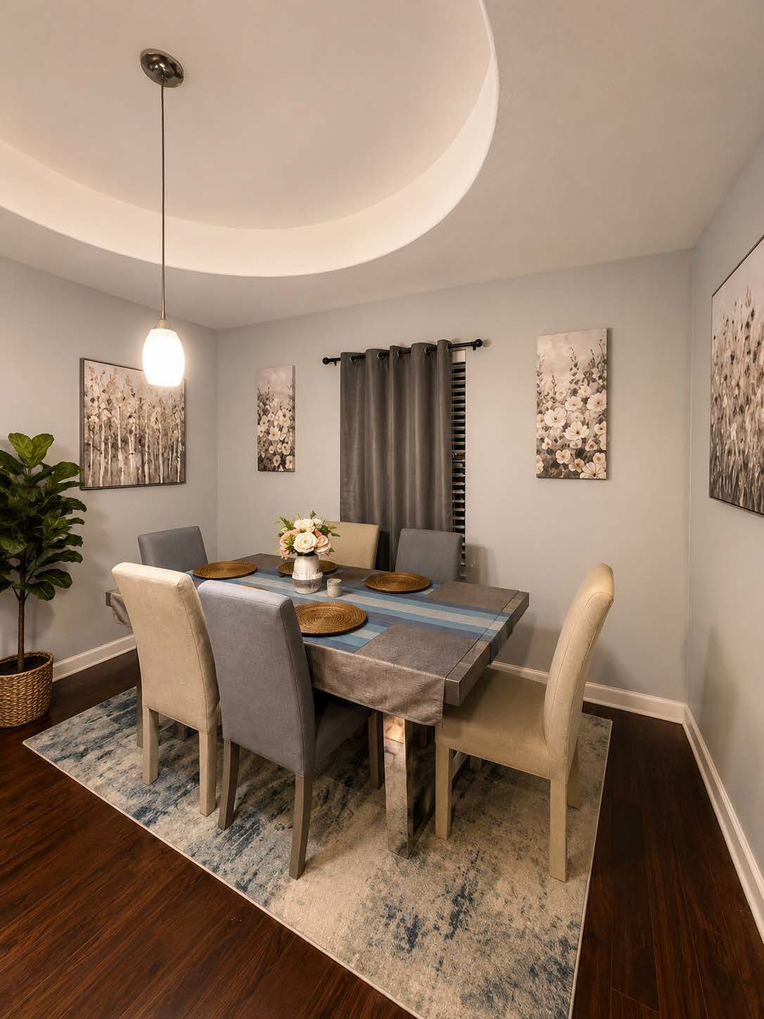 A dining area with a table set for four, a hanging light fixture, and wall art.