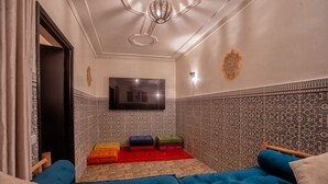 A room with a blue sofa, a flat-screen TV mounted on the wall, and patterned tiles on the walls. - Riad 3ch Salon, Terrasse avec Jacuzzi ,à Jemaa El Fna (Marrakech)