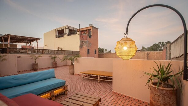 A rooftop terrace with a blue sofa, wooden benches, a hanging light fixture, and potted plants. - Riad 3ch Salon, Terrasse avec Jacuzzi ,à Jemaa El Fna (Marrakech)