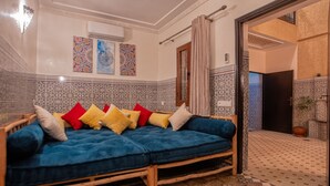 A room with a blue sofa, patterned tiles, and a door leading to another area. - Riad 3ch Salon, Terrasse avec Jacuzzi ,à Jemaa El Fna (Marrakech)