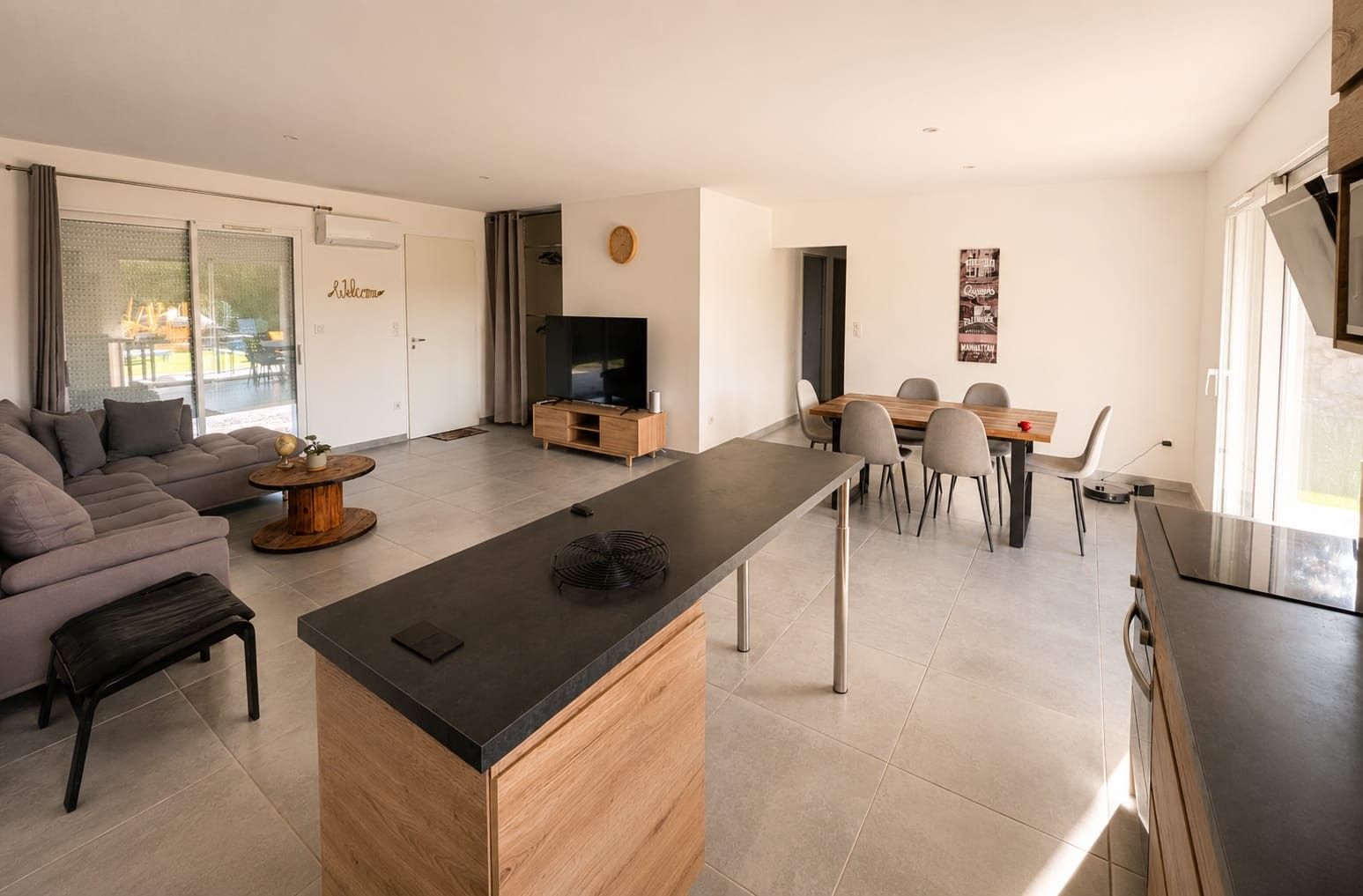 A modern living space with a sofa, a dining area, a kitchen island, and a television.