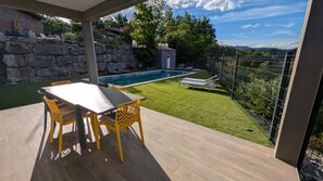 Eine Terrasse mit Tisch und Stühlen, ein Swimmingpool und Blick auf die umliegende Landschaft.