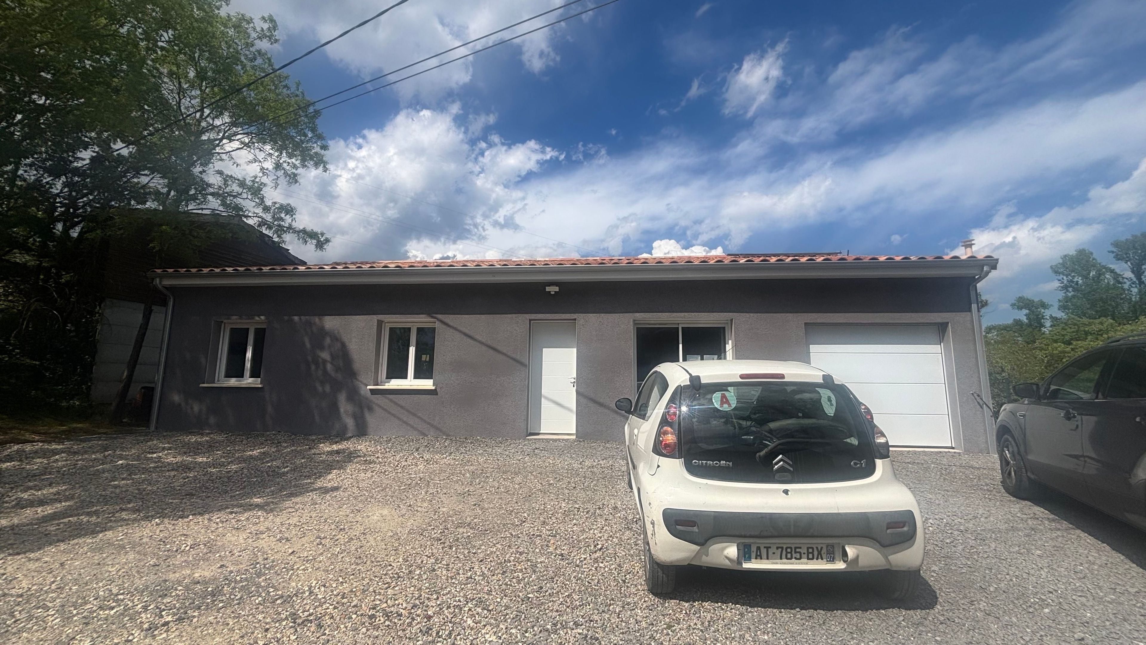 A single-story building with a gravel driveway and a parked Citroen C1 car in front.