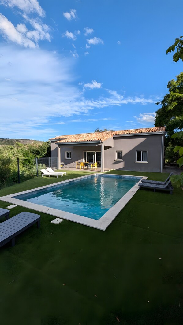Una casa moderna con piscina, patio con sedie e vista sul paesaggio circostante.