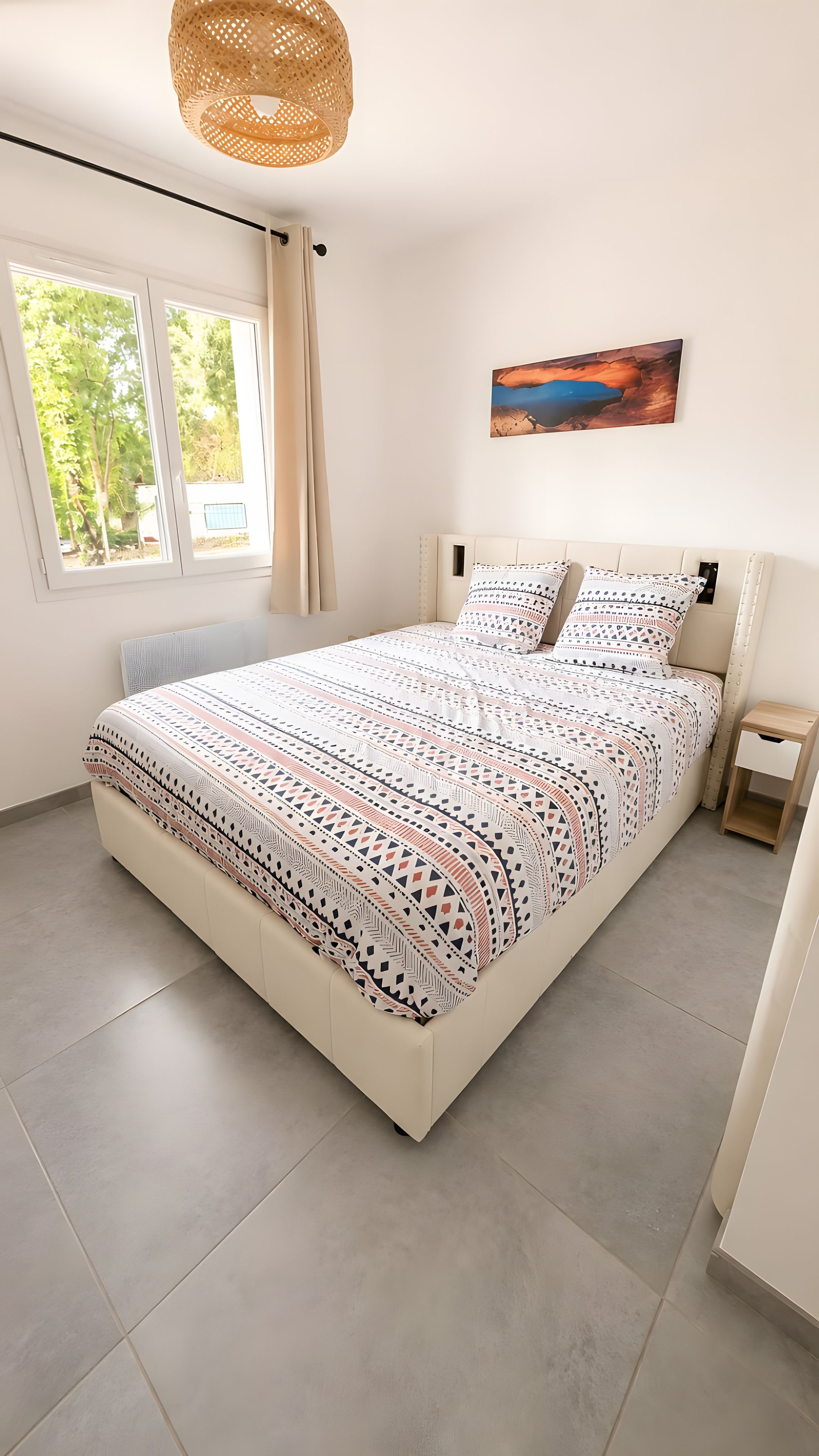 Ein Schlafzimmer mit einem großen Bett, einem Fenster, einem Gemälde und einem Nachttisch.