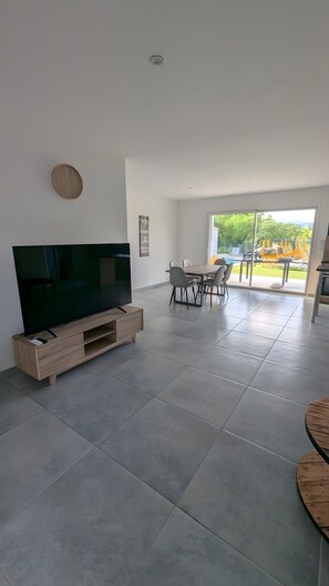 A modern living room with a flat-screen TV, a dining table with chairs, and a large window offering a view of the outdoors. - Villa 'Des Rives Et Chevaux 07' with Private Pool, Wi-Fi and Air Conditioning (Montréal)