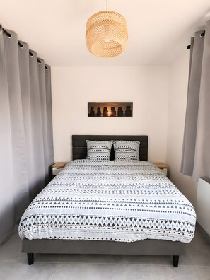 Ein Schlafzimmer mit einem Bett, einer Pendelleuchte, Wandbild und Vorhängen.