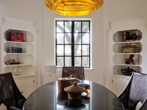 Un comedor con una mesa redonda, cestas de mimbre y estanterías llenas de libros y objetos decorativos.