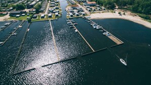 Vue aérienne d’une marina avec des bateaux amarrés, une voie navigable et une zone résidentielle avec des maisons et de la végétation.