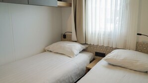 Une chambre avec deux lits simples, une table de chevet, une prise de courant et une fenêtre avec des rideaux légers.