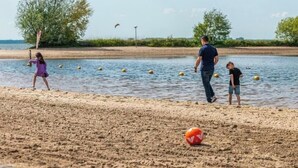 Une plage avec un filet de volley-ball, un ballon de volley-ball et des gens qui jouent.