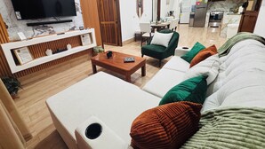 En stue med TV, sofa, sofabord og et køkken i baggrunden.