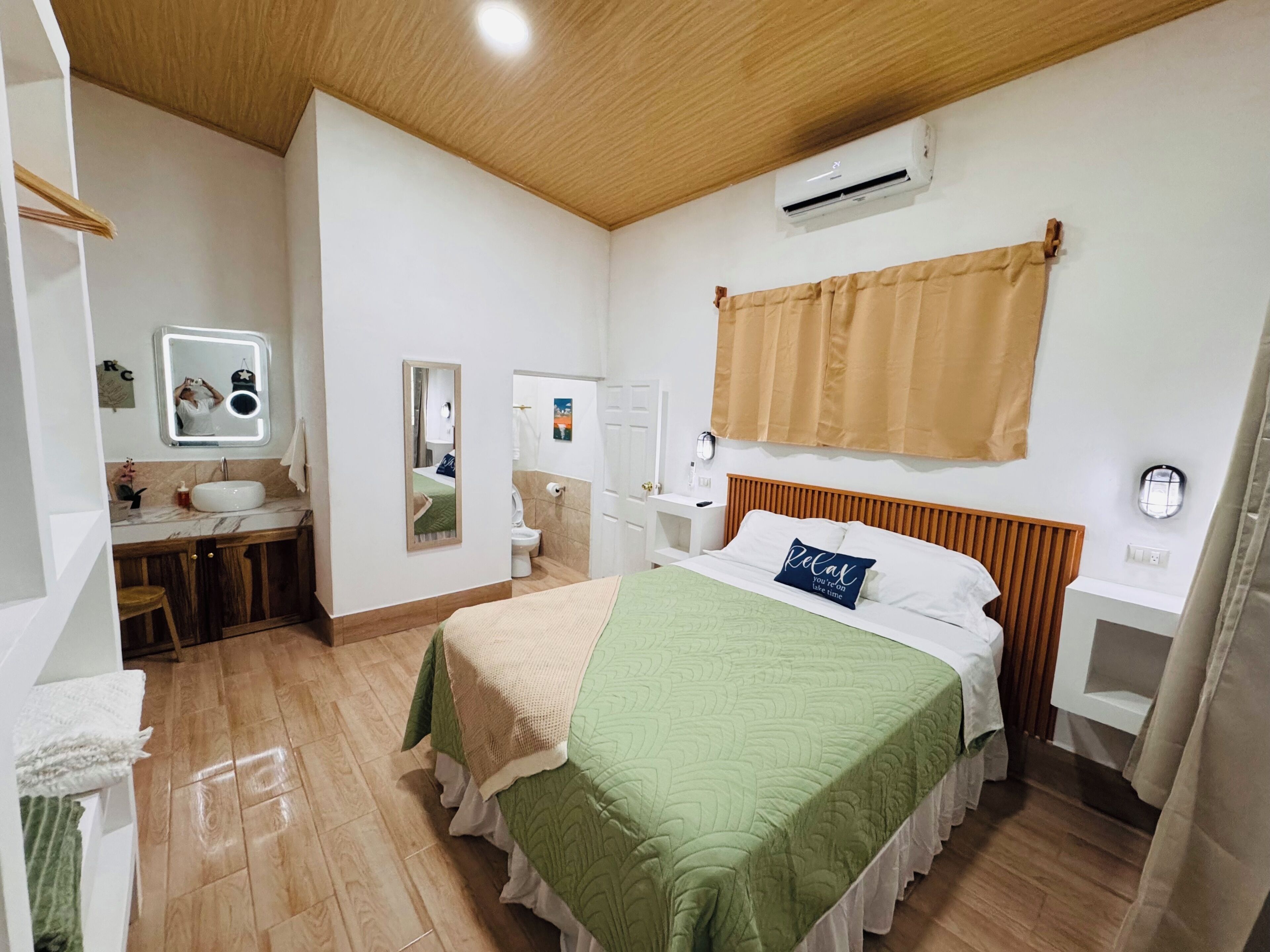 A bedroom with a bed, a bedside table, a mirror, a vanity with a sink, and an air conditioning unit.