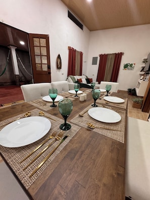 A dining area with a wooden table set for four, including plates, cutlery, and green glassware.