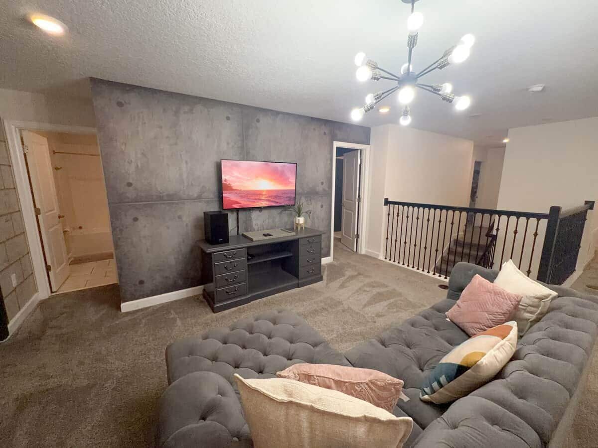 A living room with a grey sofa, a flat-screen TV on a stand, and a ceiling light fixture.