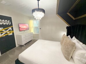 Ein Schlafzimmer mit einem Bett, einer Kommode, einem Fernseher, einer Chandelieber und einer Wand mit dem Schild 'DEEP WHITE'.