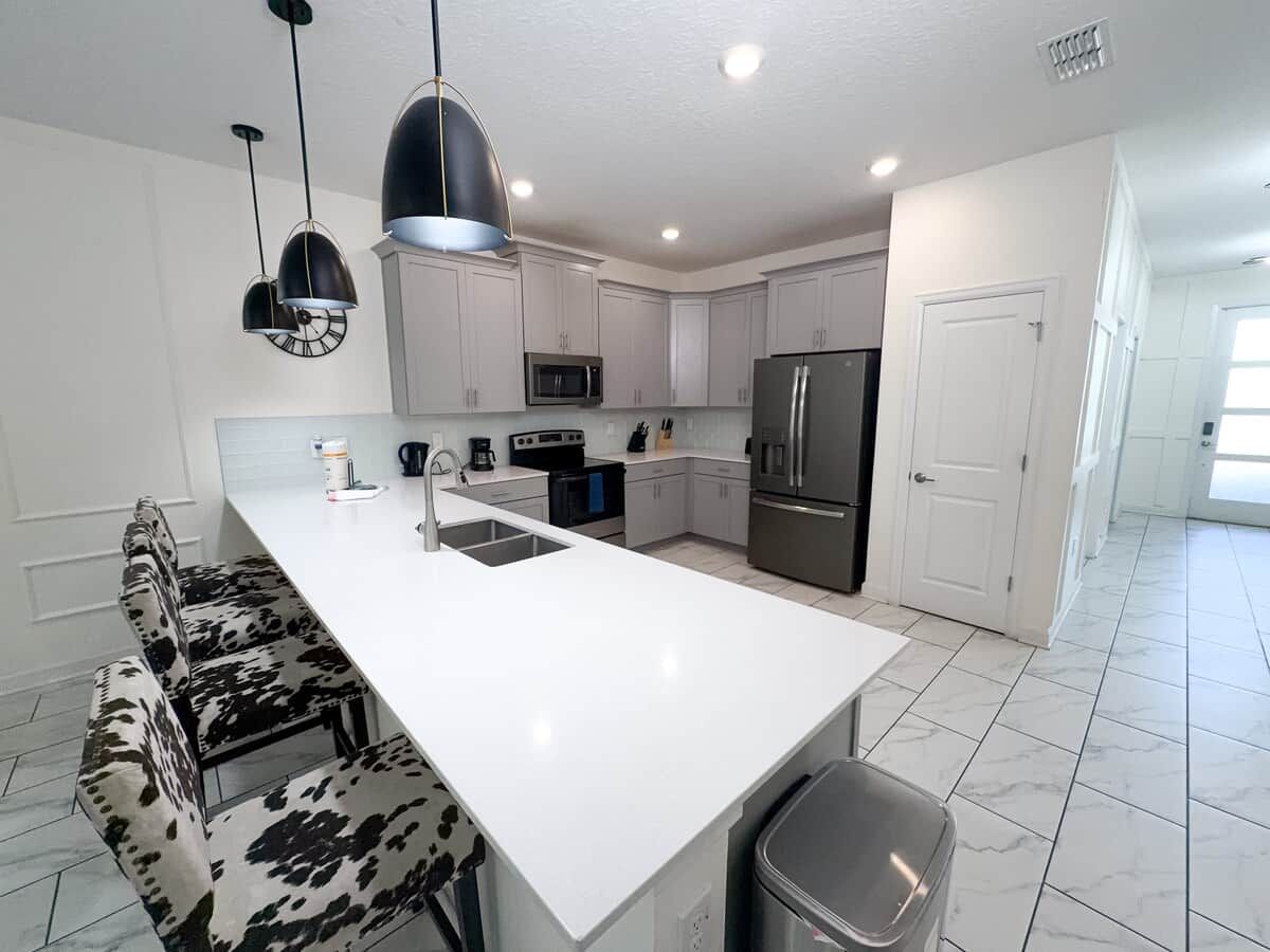 A modern kitchen with white cabinetry, a large island, and a dining area with a cow-print bench.