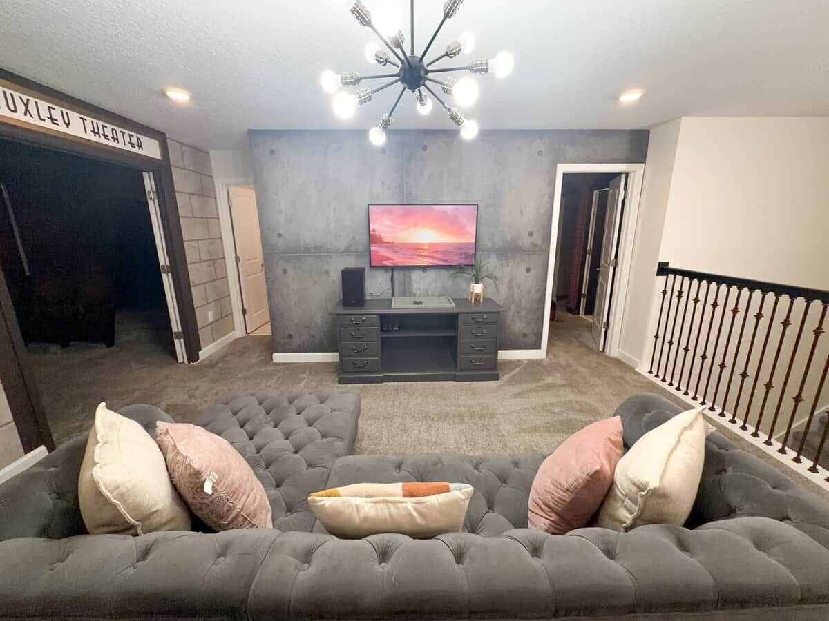 Een woonkamer met een grijze modulaire bank, een flatscreen televisie op een meubel, een open haard en een trap met een leuning.