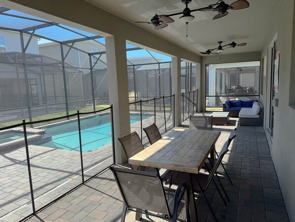 Eine überdachte Terrasse mit Pool, Sitzgelegenheiten im Freien und Deckenventilatoren.
