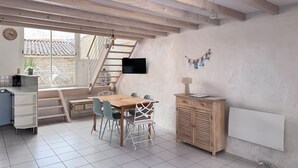 A room with a wooden staircase, a dining table with chairs, a TV mounted on the wall, and a radiator. - Maison de la Sau (Saint-Georges-d'Oléron)