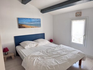 Ein Schlafzimmer mit einem Bett, einem Strandbild, einem Fenster und einer roten Lampe.