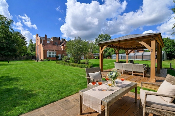 A well-maintained lawn, outdoor seating area with wicker furniture, and a brick house in the background.