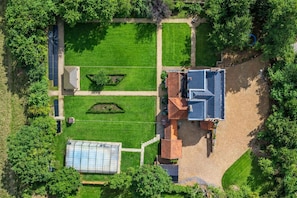 An aerial view of a property with a greenhouse, a courtyard with geometric landscaping, and a building with a sloped roof.