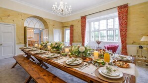 A long dining table set for a meal with floral centerpieces, candles, and a chandelier.