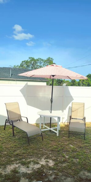 An outdoor seating area with a table and two chairs, a red umbrella, and a white fence. - Charming bedroom with kitchen (Spring Hill)