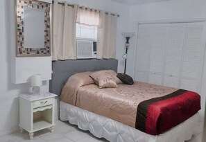A bedroom with a bed, a nightstand, a mirror, a window with curtains, and a wardrobe. - Charming bedroom with kitchen (Spring Hill)