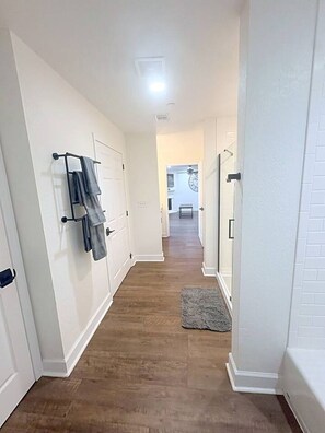 A hallway with white walls, a wooden floor, and a gray rug. There are doors on both sides, and a towel rack on the left. - Relaxing 2BR w/ AC, WiFi · Canyon Lake #420 (Canyon Lake)