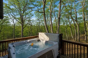 Een hottub op een houten terras met uitzicht op een bos.