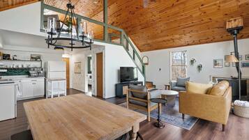 A spacious living area with a wooden ceiling, a dining table, a sofa, and a TV.
