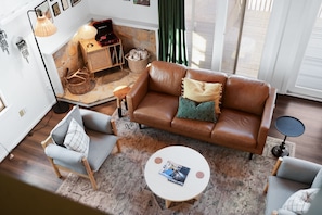 Een gezellige woonkamer met een bruine leren bank, twee fauteuils, een klein rond tafeltje en een rieten mand.
