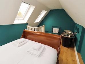 A bedroom with a wooden bed, two skylights, a white crib, and a black trash bin. - 9 Longhirst Village (Morpeth)