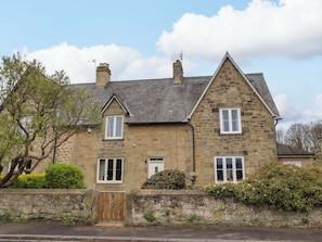 A stone house with a traditional design, featuring a stone facade, a wooden gate, and a well-maintained garden. - 9 Longhirst Village (Morpeth)