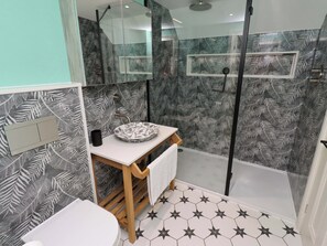 Ein modernes Badezimmer mit Duschkabine aus Glas, einem weißen Waschbecken mit dekorativer Schale und einer Toilette.
