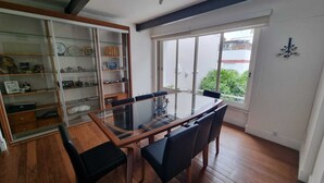 A dining area with a glass-top table, black chairs, and a sliding glass door leading to a balcony with a view of greenery.