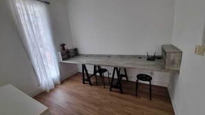 Uma cozinha pequena com bancada de madeira, três bancos e uma janela com cortinas leves.