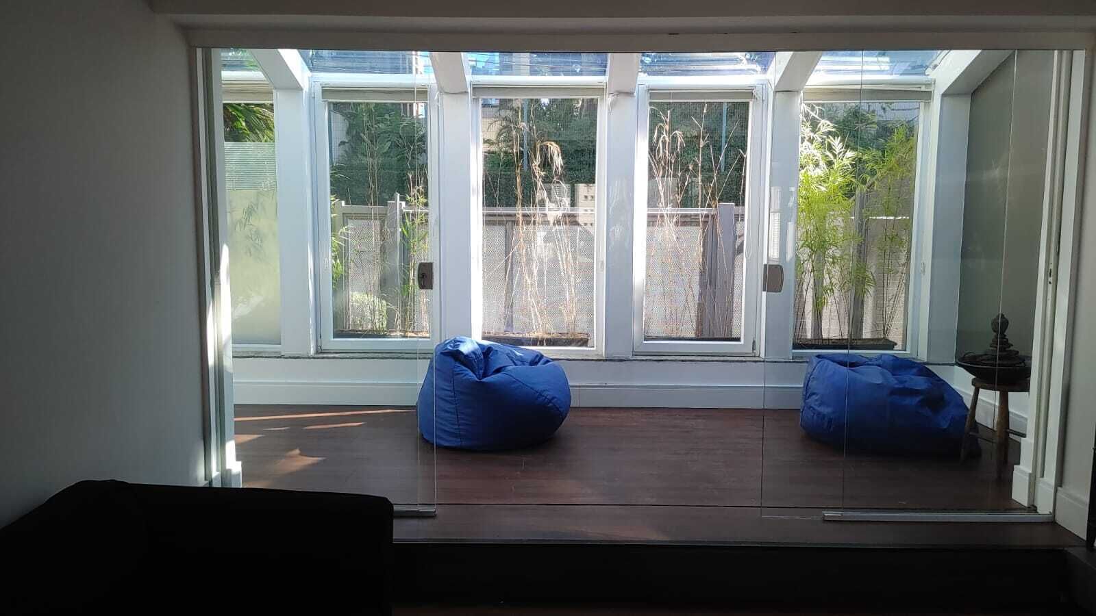 Quarto com uma grande porta de vidro que dá para área externa, dois sacos de poltrona azuis e uma pequena mesa com um objeto decorativo.