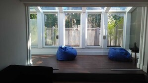 A room with a large glass door leading to an outdoor area, two blue bean bags, and a small table with a decorative item.