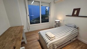 A bedroom with a bed, a bedside table, a lamp, a window, and a shelf.