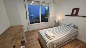 A bedroom with a bed, a bedside table, a lamp, a window, and a shelf.